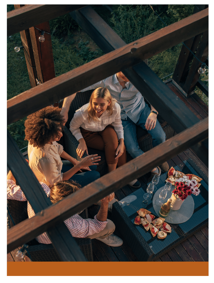 Friends enjoying an outdoor seating area under a wooden pergola, sharing food and drinks in a cozy ambiance