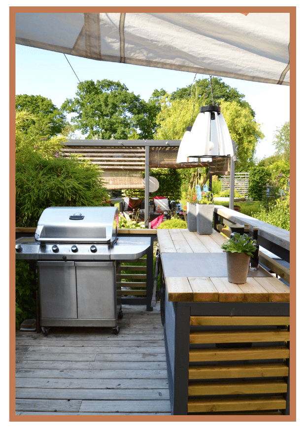 Stylish outdoor kitchen with a grill, wooden countertops, and lush greenery in the background