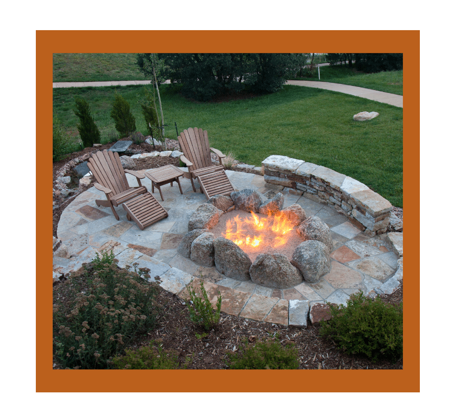 Beautiful stone fire pit with flames surrounded by wooden Adirondack chairs on a landscaped patio.