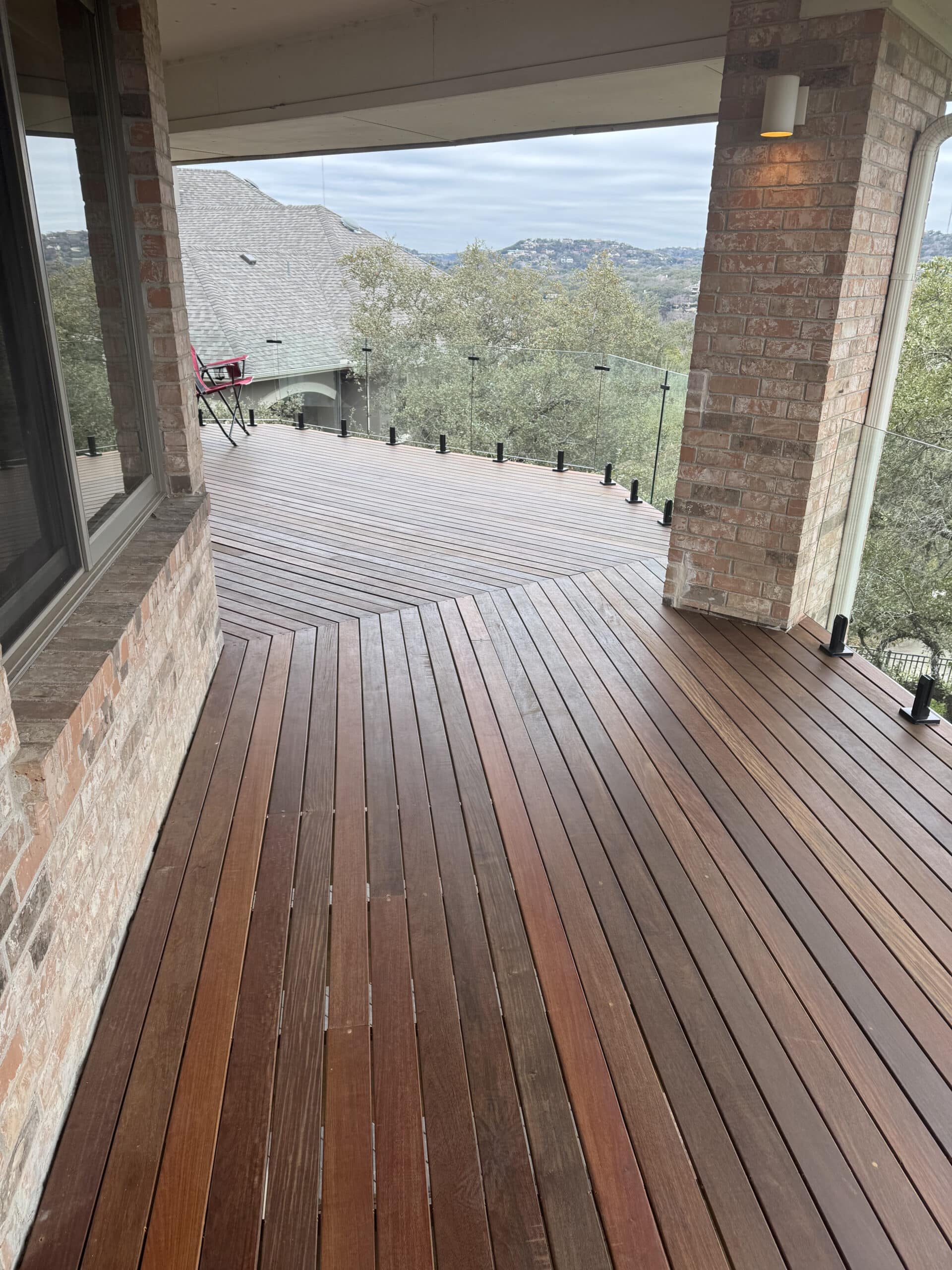 Elevated wooden deck with glass railing and brick pillars offering a low-maintenance scenic outdoor area