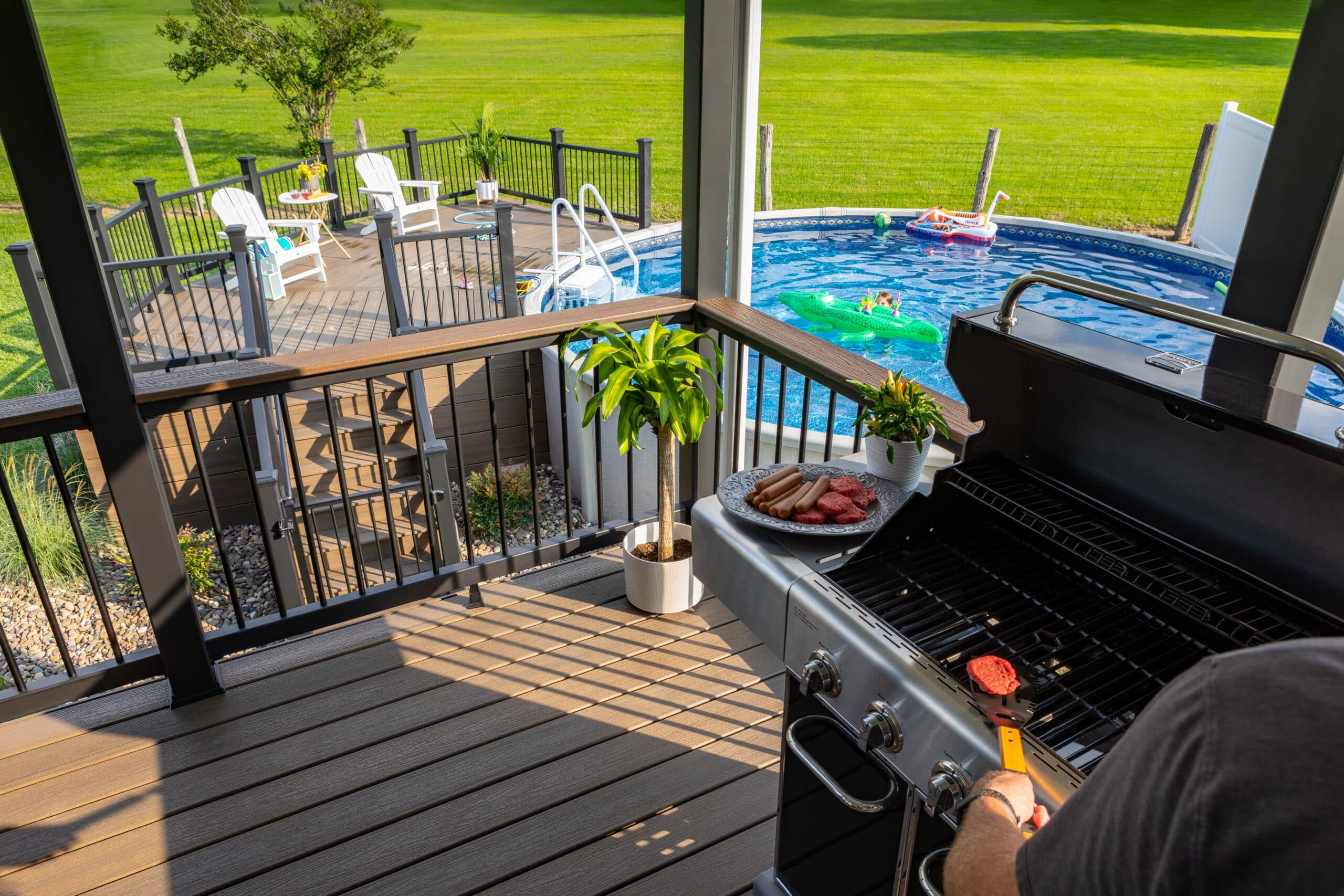 Elevated grilling area and round pool surrounded by TREX composite decking in a landscaped backyard